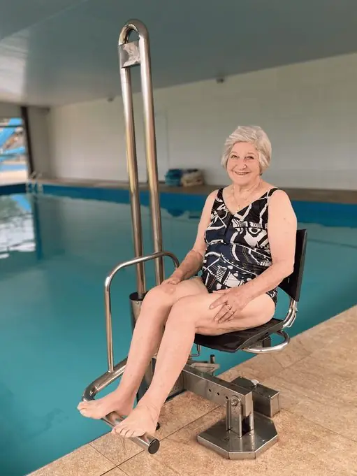 Usuária sentada na cadeira, em piscina coberta
